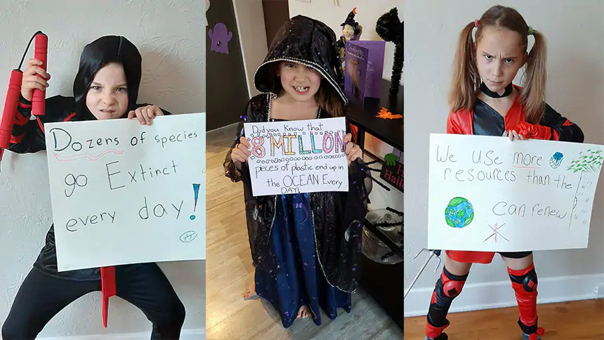 Three kids in costumes hold signs with environmental messages on them.