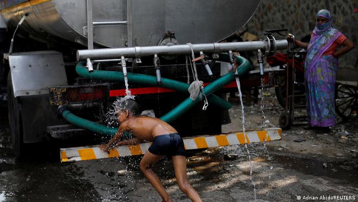 A boy wants to cool down in a jet of water under a tanker truck that supplies water to urban areas. 
