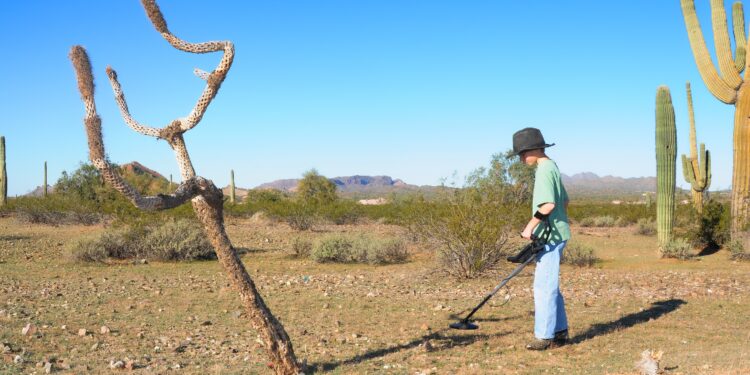 A boy explores the desert with a metal detector.