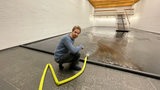 A man leans on the floor and uses a hose to pour water into a room.