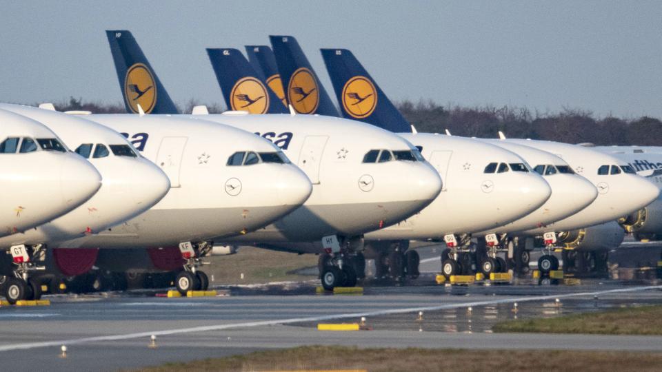 A row of Lufthansa planes parked next to the runway.