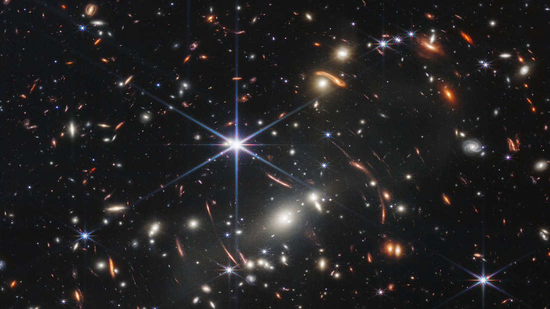 The first image from the James Webb Telescope to be presented: a so-called dark field over which hundreds or thousands of galaxies can be seen.  Thanks to a microlensing effect (the gravity of a galaxy cluster in the foreground magnifies the galaxies in the background), 
